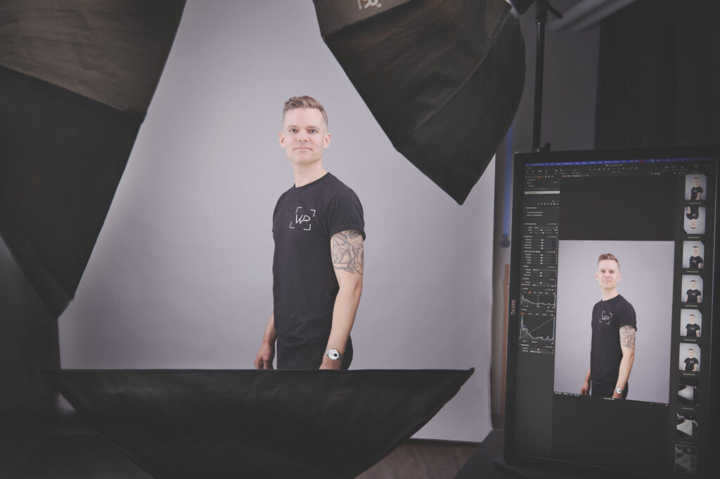 Behind-the-scenes i fotostudie med fotograf ved Lightroom-computer og softboxes i baggrunden
