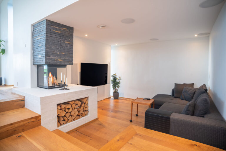 Moderne stue med trægulve, en mørkegrå sektionssofa, et fladskærms-tv og stilfulde Airbnb-detaljer - en potteplante og en dobbeltsidet pejs med stablet brænde under og stearinlys ovenpå - perfekt til enhver fotografs portefølje.