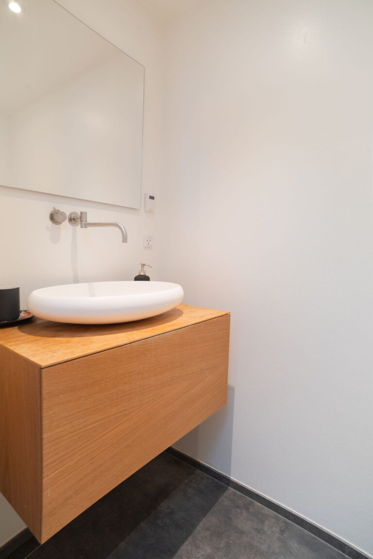 Minimalistisk badeværelse, der er perfekt til en Airbnb-annonce, med en flydende trævask, rund hvid vask, væghængt vandhane, sæbedispenser og stort spejl - ideelt til enhver fotograf, der søger moderne enkelhed.