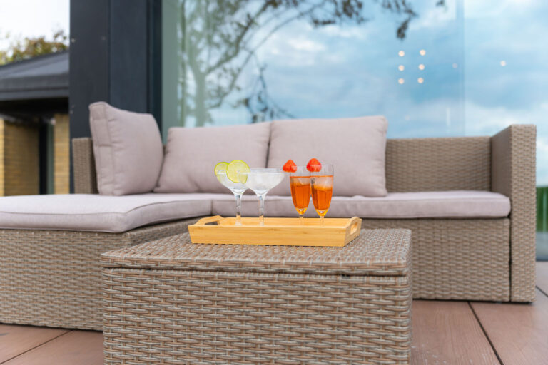 Fanget af en dygtig fotograf til en indbydende Airbnb-annonce, viser et udendørs sofabord i flet to cocktails med lime- og appelsindrinks med jordbær foran en beige hyndesofa på terrassen.