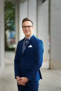 Professionelt portræt af mand i mørkeblåt jakkesæt og briller, taget udendørs i en urban ramme. Ideelt til LinkedIn og erhvervsmæssige profiler. Fotograferet af Weigang Fotografi, specialister i medarbejderportrætter og erhvervsfotografi i København.