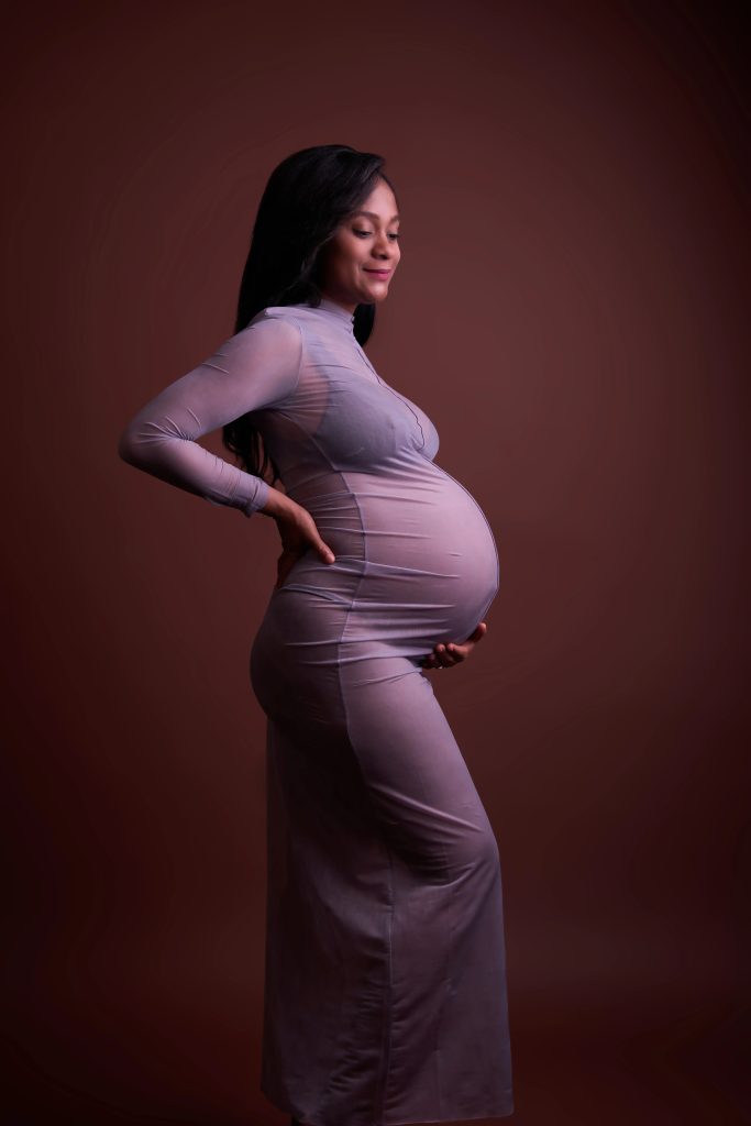 Gravid kvinde i lyseblå sheer kjole set fra siden, varmt baggrundslys i studie