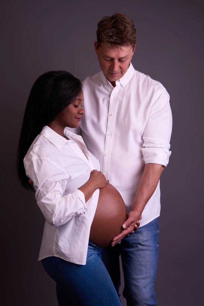 Gravid kvinde og hendes partner i hvide skjorter holder om hendes mave, intimt graviditetsfoto i studie