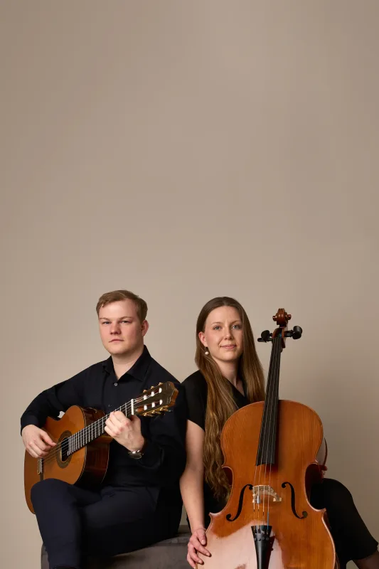 Jonas og Monica sidder roligt side om side med deres instrumenter og kigger direkte i kameraet. Seriøst og stilfuldt portræt med meget luft over motivet.