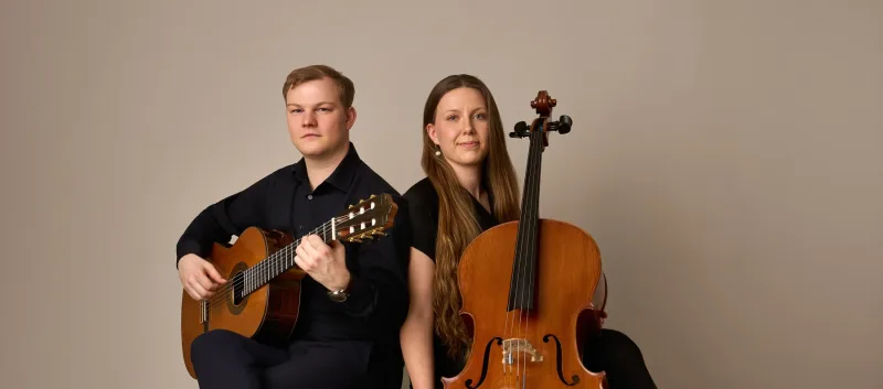 Bredt duo-portræt af Jonas og Monica med deres instrumenter. Begge kigger frem mod kameraet med et afslappet og professionelt udtryk. Velegnet som bannerbillede.